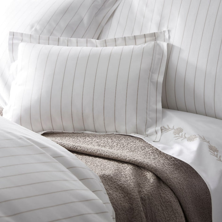 Close-up of Matouk Amalfi striped pillows and embroidered blanket on a bed.