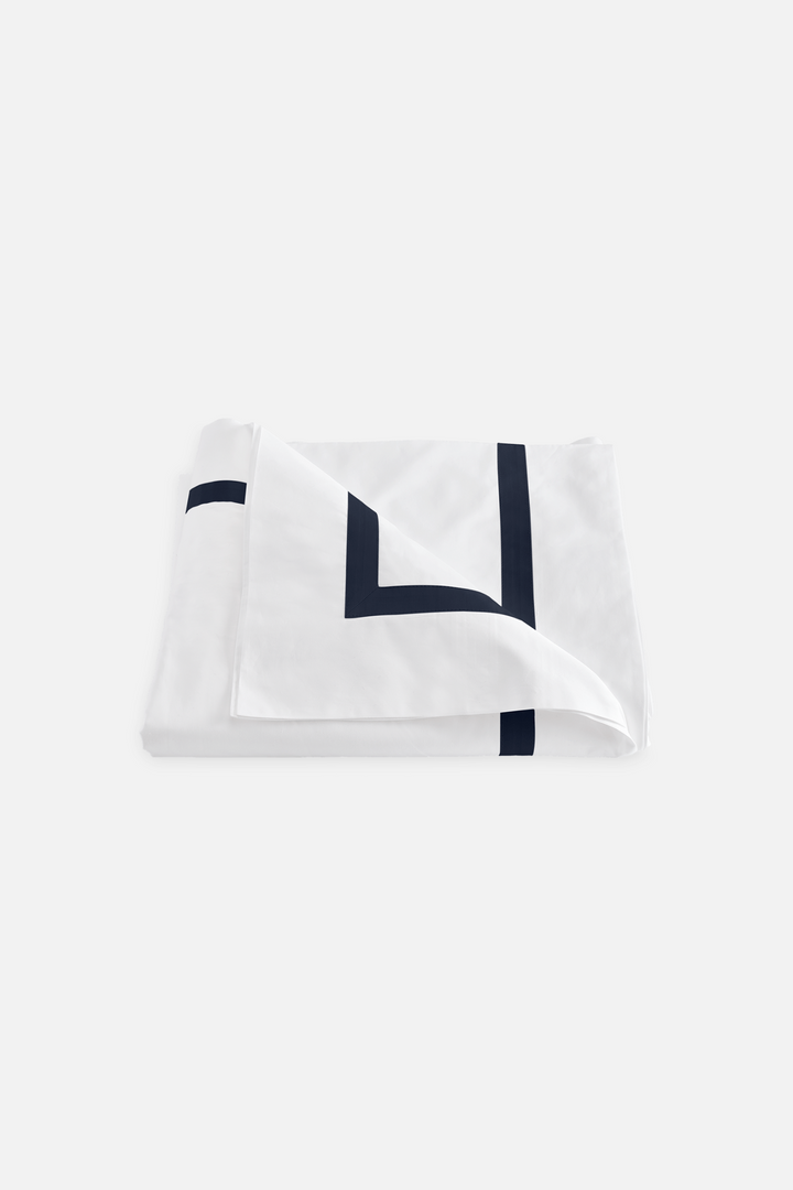 A folded Lowell duvet cover in navy color with a sateen border on a white background.