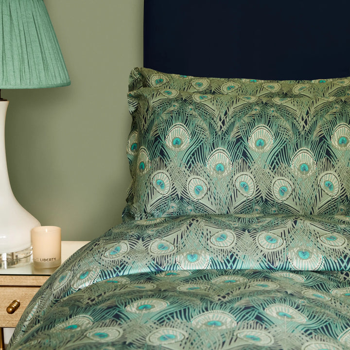 Liberty London Hera bedset in jade peacock on a bed next to a bedside table with a candle