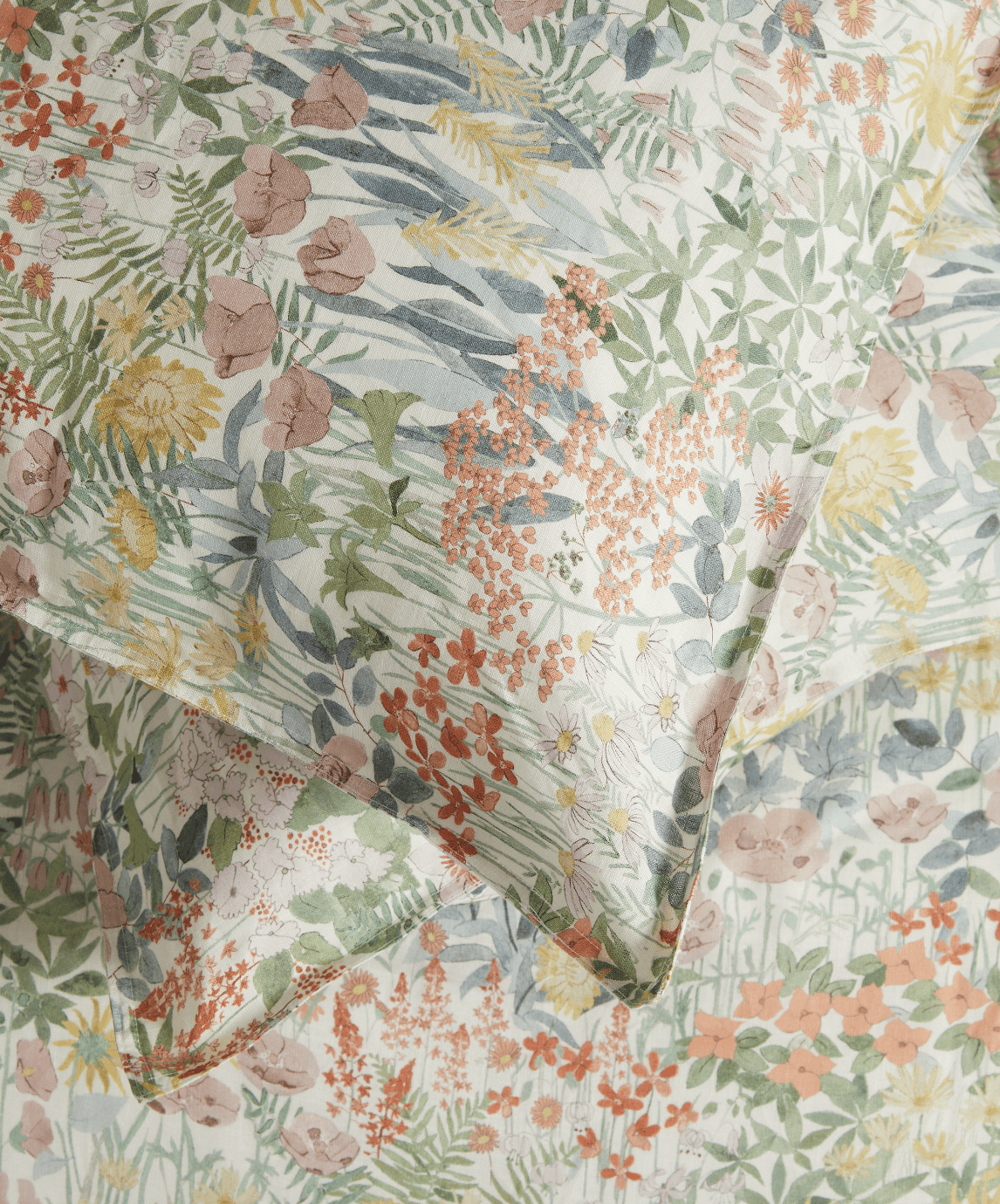 Close up of the Liberty London Faria pillow lying on another pillow and matching Faria print sheet