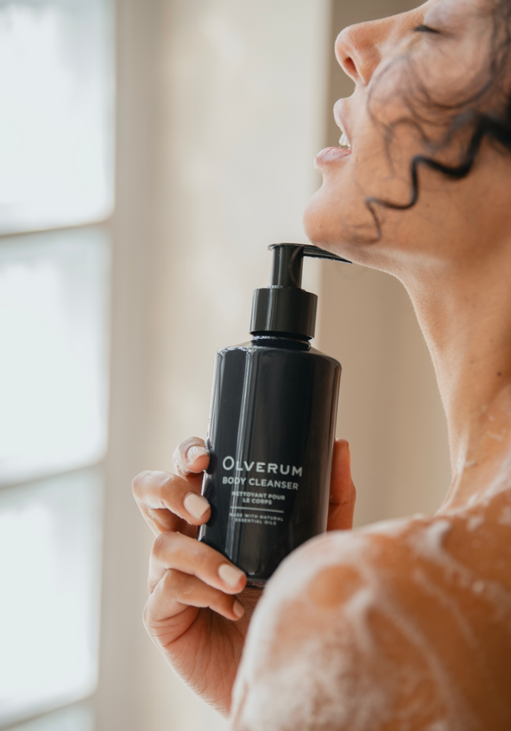 Person holding an Olverum body cleanser bottle with a blurred background