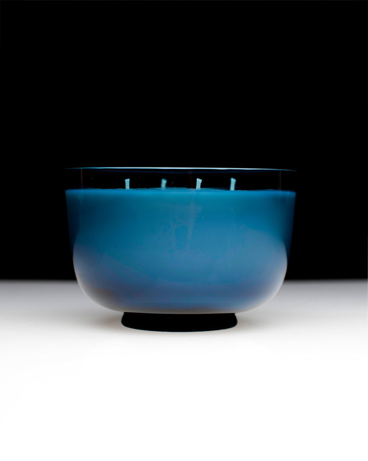 Blue candle in a glass holder on a white surface with a black background Serax Vincent van Duysen