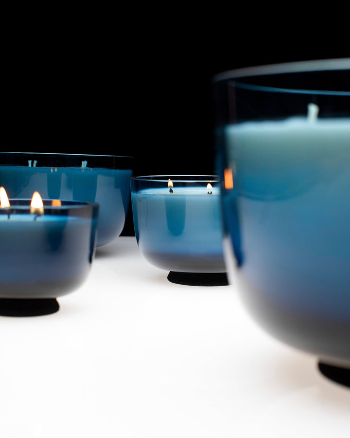 Blue candles in glass holders on a white surface with a black background Serax Vincent van Duysen