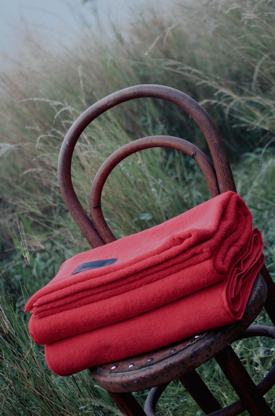 Red blanket on a wooden chair in a grassy field