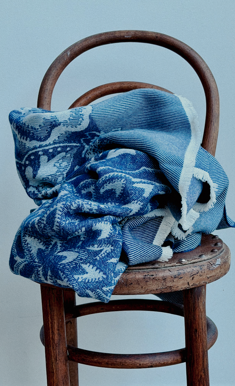 A blue and white patterned fabric accessory, possibly a scarf or throw, draped over a rustic wooden chair against a light gray background.