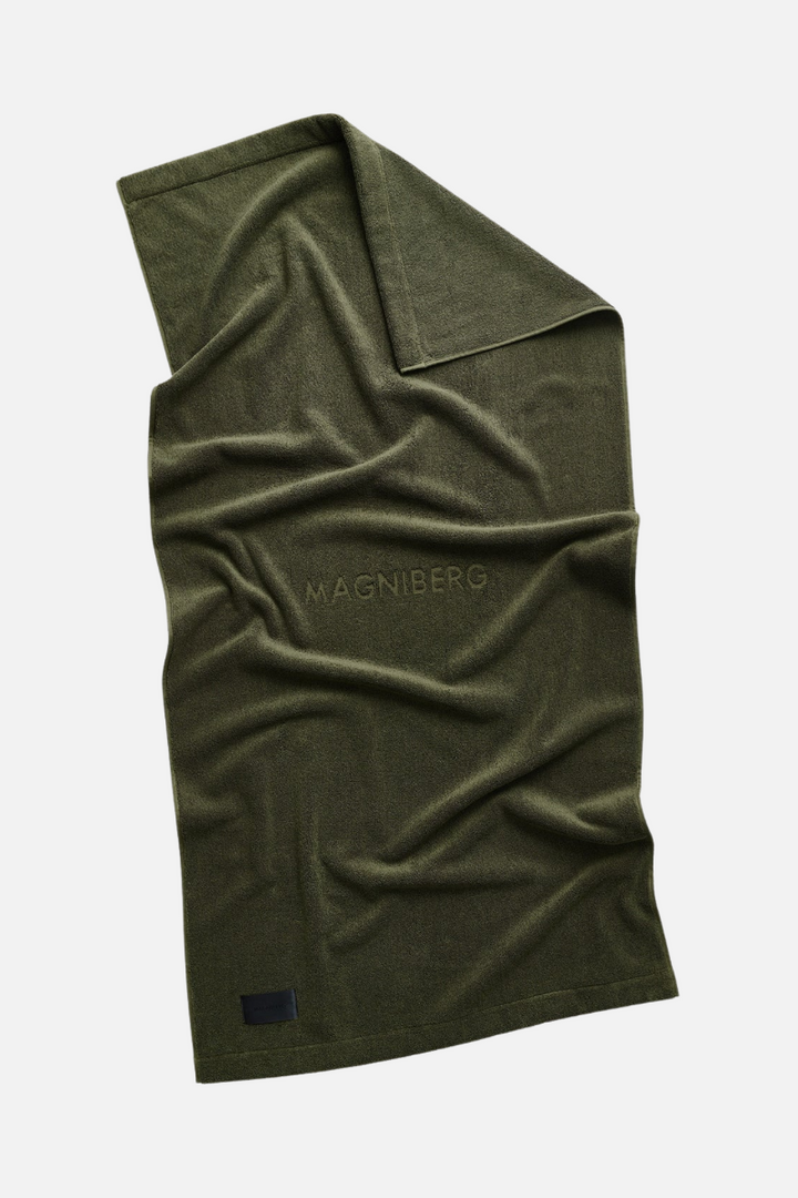 Olive green bath towel with 'MAGNIBERG' branding on a white background